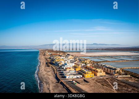 Vista aerea di un villaggio costiero con case bianche e gialle che costeggiano la riva, saline nell'entroterra, Cabo de Gata, Spagna Foto Stock