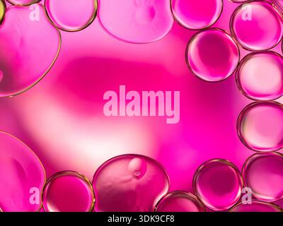 Primo piano di bolle d'olio rosa brillante che formano una sfera lucida e astratta. Le vivaci tonalità magenta e il soffice bagliore evocano energia e grafica moderna, Foto Stock