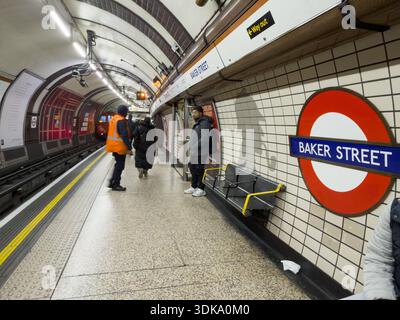 Londra, Regno Unito. 30 gennaio 2026. Trasporto per il membro del personale londinese in giubbotto ad alta visibilità con passeggeri sulla piattaforma della linea Bakerloo della stazione della metropolitana di Baker Street, cartellonistica tradizionale TfL in primo piano dopo la rimozione notturna della campagna pubblicitaria Heineken 'Bakerl0.0 line'. Le operazioni della stazione sono tornate ai protocolli standard TfL e di personale dopo due settimane di campagna commerciale temporanea che ha generato polemiche da parte del gruppo di sostegno alla disabilità sui problemi di wayfinding. Credito: Glosszoom/Alamy Live News Foto Stock
