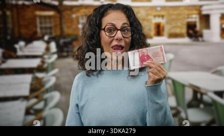 Donna sorridente all'aperto sulla terrazza di un ristorante che tiene in mano banconote della corona islandese, raffigurante la mezza età, il denaro, la valuta, la finanza, atmosfera allegra. Foto Stock