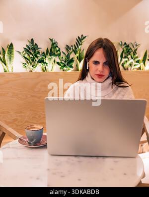 Donna che lavora su un computer portatile e beve caffè in un bar Foto Stock