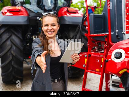 Dirigente donna con tablet che offre stretta di mano con macchinari agricoli Foto Stock