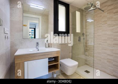 Bagno dal design contemporaneo con piastrelle beige, doccia in vetro e lavandino a parete Foto Stock