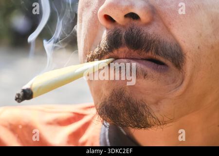 Primo piano di un uomo rilassato che fuma marijuana. Fumo bianco proveniente dalla bocca di una persona che usa cannabis per scopi ricreativi o medici Foto Stock