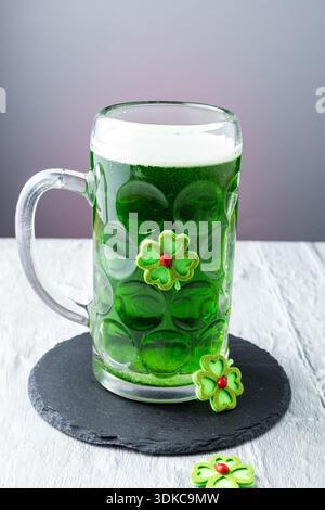Birra verde versata in una tazza di vetro con decorazione shamrock per la celebrazione del giorno di San Patrizio. Birra irlandese festiva con schiuma, movimento e c Foto Stock