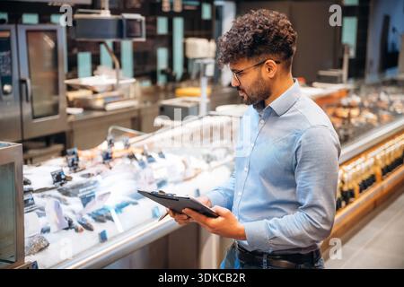 Blocco note nero nelle mani. Un lavoratore maschile è nel negozio di alimentari. Foto Stock