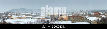 Lo skyline della città vecchia di Leopoli con la torre del municipio e la torre Korniakt durante la tempesta di neve invernale. Paesaggio urbano panoramico dei monumenti storici del centro storico sotto lo spessore Foto Stock