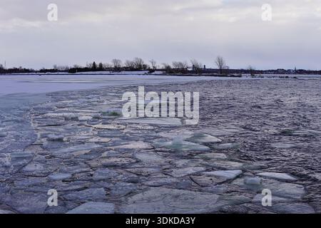 Frammenti di ghiaccio galleggianti su un fiume scuro in inverno. Consistenza d'acqua congelata con una costa lontana sotto un cielo grigio. Foto Stock
