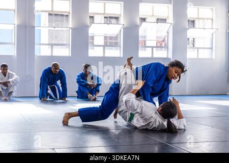 Diverse partner di allenamento femminili che praticano la lotta su tappetini imbottiti presso la palestra di arti marziali con gis. Arti marziali, fitness, atletismo, allenamento, lavoro di squadra, resilienza, disciplina || modello rilasciato Foto Stock