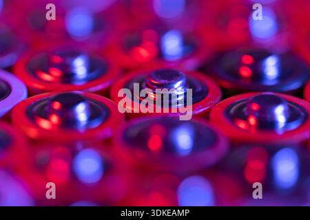 Primo piano delle estremità positive delle batterie scariche dimensioni AA, scatto macro, messa a fuoco selettiva. Batteria alcalina usata. Concetto di spazzatura pericolosa. Luce blu e rossa al neon Foto Stock