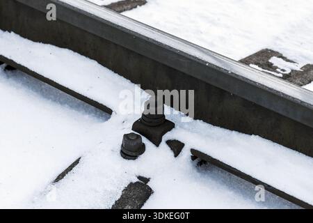 Un primo piano di bulloni innevati e rotaie in acciaio, che catturano un freddo momento industriale su una ferrovia. La struttura invernale e l'infrastruttura robusta sono in grado di trasmettere Foto Stock