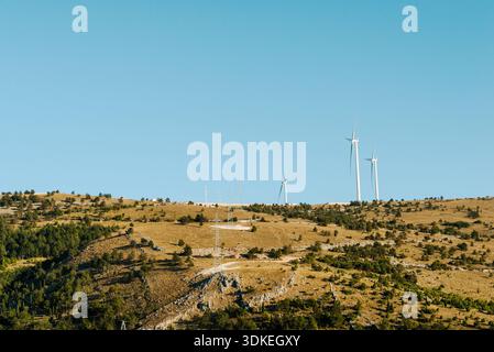 Turbine eoliche sul paesaggio montano che producono energia rinnovabile, produzione di energia pulita in aree rurali sotto il cielo azzurro. Foto Stock