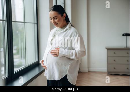 La donna incinta è a casa in una stanza domestica. Foto Stock