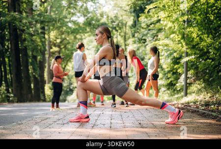 Esercizio di stretching da parte di una donna. Un gruppo di corridori si trova all'aperto. Foto Stock