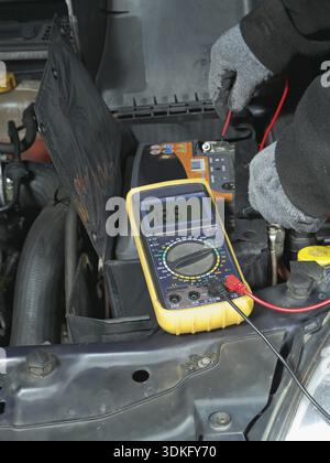 Auto meccanico auto misura la tensione della batteria usando un multimetro Foto Stock