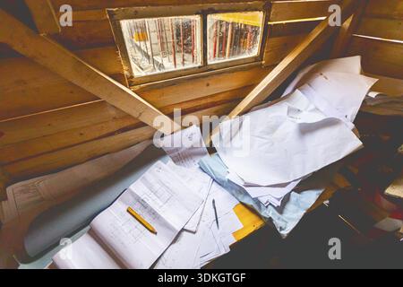 La scrivania di Mason in una cabina di legno con una pila di disegni architettonici, layout di carta e planimetrie. Piccola finestra con vista sul cantiere Foto Stock
