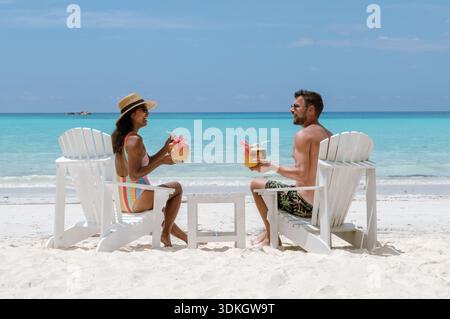 Coppia che si gode una giornata di sole alla spiaggia di Grand Anse a Praslin, Seychelles. Si rilassano sulle sdraio, sorseggiando cocktail tropicali, circondati da Foto Stock