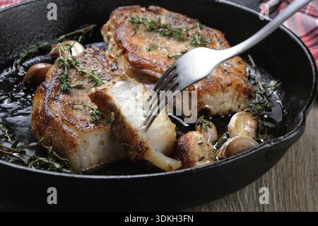 Cibo, Una fetta di bistecca di maiale tagliata con olio fritto con aglio ed erbe aromatiche un pezzo in una padella. Primo piano Foto Stock