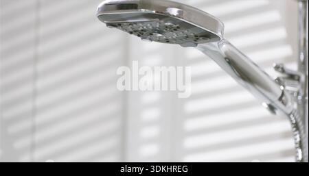 L'acqua scorre da una doccia in un bagno con luce solare che splende attraverso le tende al mattino Foto Stock