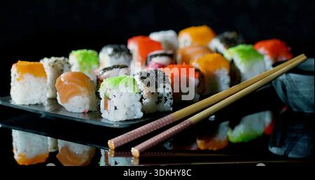 Collezione di sushi dai colori vivaci, sapientemente posizionati su una base scura lucida con illuminazione soffusa per creare un'atmosfera accogliente Foto Stock