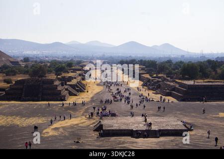I turisti camminano lungo Avenue of the Dead nel sito archeologico di Teotihuacan con antiche rovine e piramidi sotto il cielo nebuloso, Messico Foto Stock