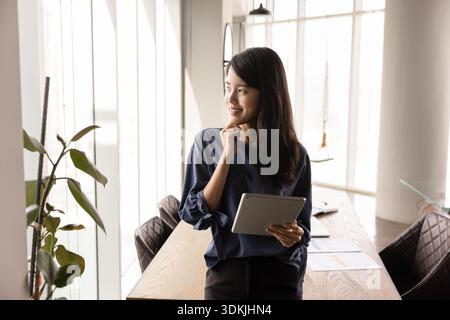 Felice e premurosa giovane donna asiatica che detiene un tablet pc Foto Stock