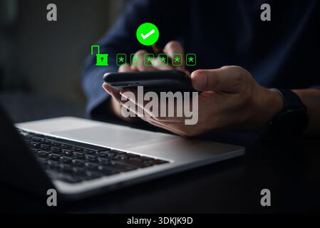 Concetto di sicurezza informatica con l'uomo che utilizza lo smartphone per l'autenticazione a due fattori e la verifica dell'accesso tramite password vicino al laptop, la protezione dei dati digitali e. Foto Stock