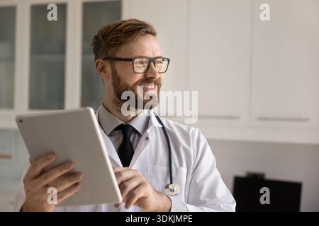 Giovane medico di successo sorridente che tiene da parte il pad digitale Foto Stock