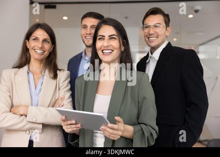 Una donna d'affari ispanica felice regge un tablet digitale in posa con diversi compagni di squadra Foto Stock