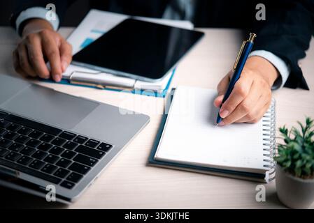 Business, Writing Manager prende appunti alla scrivania di un ufficio con laptop e penna, organizzando pianificazione, report, dati e analisi per acquisire idee, attività, Foto Stock