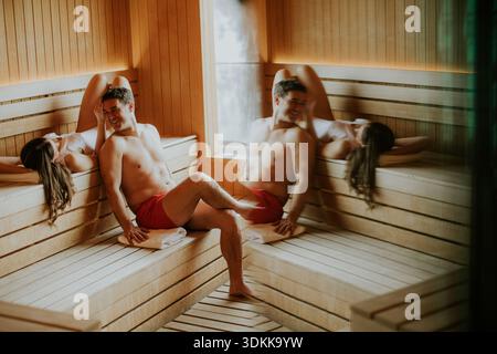 Due amici si siedono in una sauna godendosi la compagnia dell'altro dopo un allenamento. Sorridono e chiacchierano seduti sulle panchine di legno nel caldo di Foto Stock