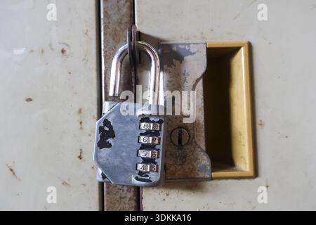 Vista ravvicinata del lucchetto a combinazione in metallo che fissa una vecchia porta dell'armadietto arrugginita. forgotten lock fornisce un senso di sicurezza, privacy e protezione per Foto Stock
