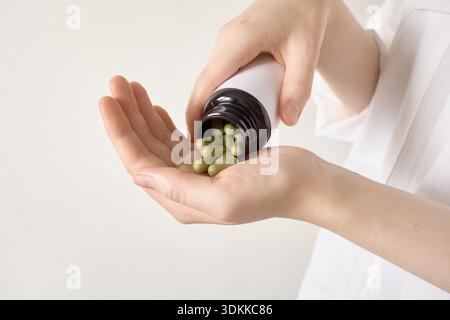 Mani che versano capsule di erbe verdi dalla bottiglia in un palmo aperto Foto Stock