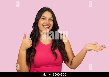 Giovane donna sorridente che mostra approvazione con i pollici in alto e la mano aperta per la presentazione Foto Stock