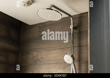 Una doccia è montata sulla parete di un bagno. L'acqua scorre dalla doccia. La parete è coperta da pannelli di legno. L'impostazione è semplice e cl Foto Stock
