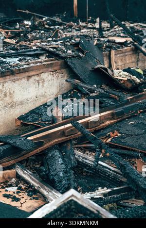 Detriti di legno carbonizzati e cenere dopo un incendio distruttivo, che mostrano materiali da costruzione bruciati e danni causati da incendio doloso o incidente. Messa a fuoco selettiva. Foto Stock