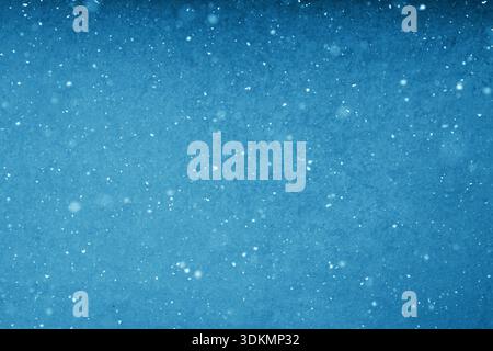 Vista minimalista full-frame dei fiocchi di neve densi che cadono delicatamente su uno sfondo invernale blu chiaro e morbido, messa a fuoco selettiva Foto Stock