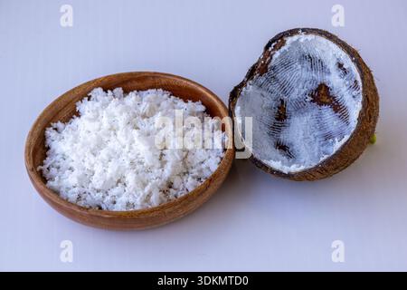 Cocco appena grattugiato in un recipiente di legno con metà guscio raschiato. Carne di cocco biologica grattugiata per la cottura e la cottura. Supercibo tropicale crudo ingerito Foto Stock