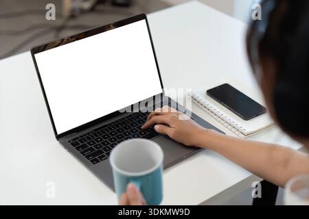 Ufficio domestico. Giovane professionista che lavora su un computer portatile con una tazza di caffè in mano. Foto Stock