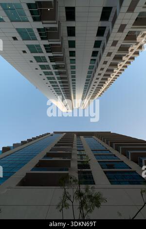 Vista simmetrica verticale ad angolo basso di due moderni grattacieli residenziali sotto un cielo azzurro Foto Stock