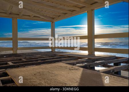 Una vista panoramica da una località balneare a San Vincenzo, Italia. Travi in legno incorniciano lo scintillante Mar Mediterraneo sotto un luminoso e caldo sole pomeridiano Foto Stock
