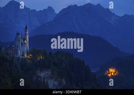 Germania. Notte estiva in Baviera. Luci di due castelli di Neuschwanstein e Hohenschwangau contro lo sfondo delle montagne boscose Foto Stock