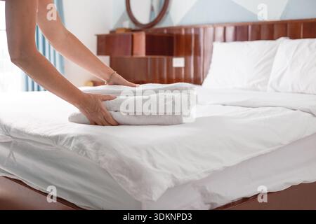 Le mani posizionano una pila di asciugamani bianchi piegati su un letto ben fatto in una camera d'albergo o in una pensione. Pulizia delle camere dell'hotel. Foto Stock