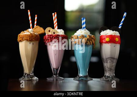 Quattro frullati colorati con diversi condimenti, tra cui biscotti e Oreo. I frullati sono serviti in bicchieri alti con cannucce colorate. L'imag Foto Stock