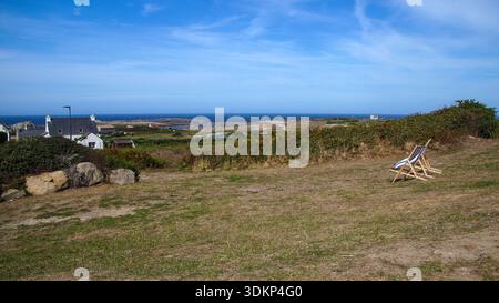 Due sedie a sdraio vuote si affacciano sul vasto mare da un tranquillo paesaggio costiero, invitante relax e solitudine sotto un cielo azzurro. Foto Stock