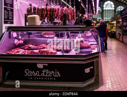 Un macellaio al Mercat Central di Valencia espone carne fresca e salsicce spagnole tradizionali appese al banco. Foto Stock