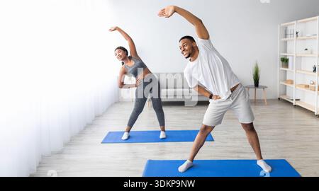 Coppia nera atletica che si piega da parte, facendo esercizi a casa, banner design con spazio libero Foto Stock