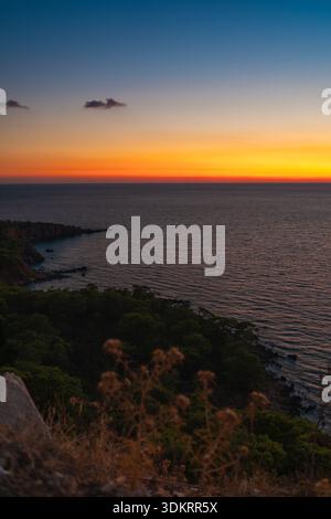Tramonto colorato sul mare calmo e sul paesaggio roccioso della costa Foto Stock