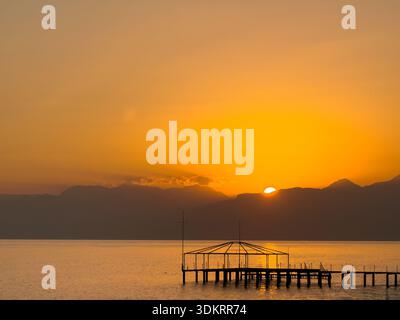Sagoma del molo in legno sul tramonto dorato sull'acqua calma Foto Stock