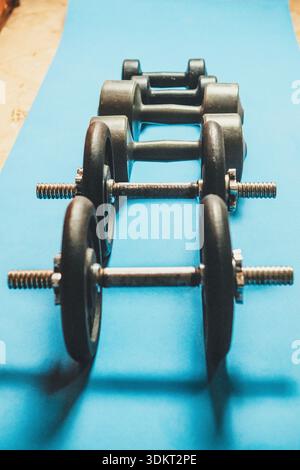 Set di manubri di vari pesi posizionati su un tappetino per il fitness di colore azzurro Foto Stock
